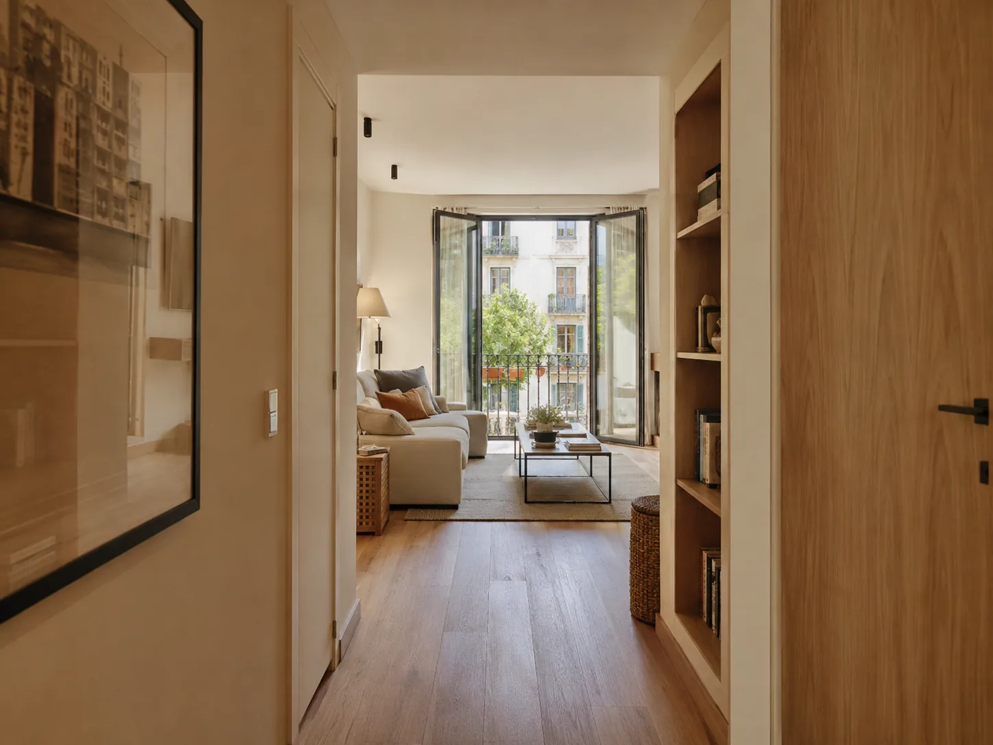 Pasillo largo de vivienda que desemboca en el salón y en una puerta de balcón.